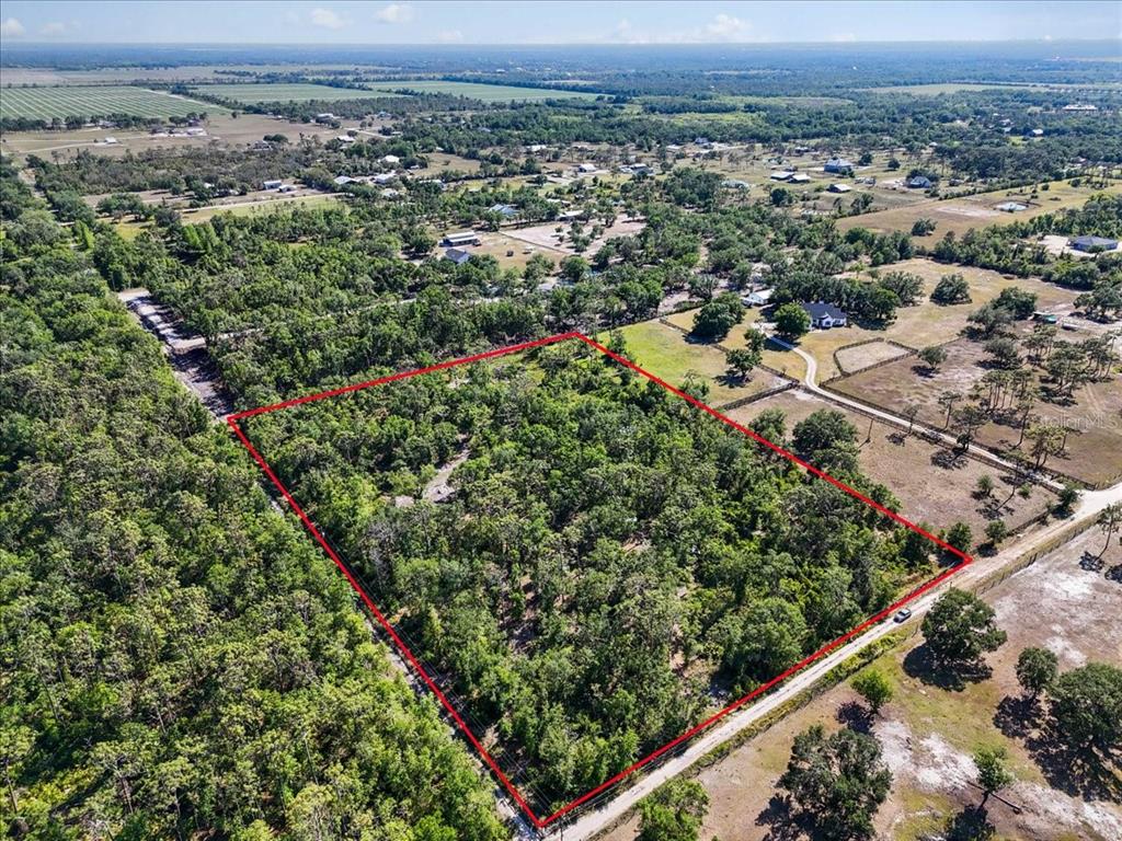 An aerial view shows a rectangular, tree-covered plot of land outlined in red — 24820 49TH AVENUE E, MYAKKA CITY, FL