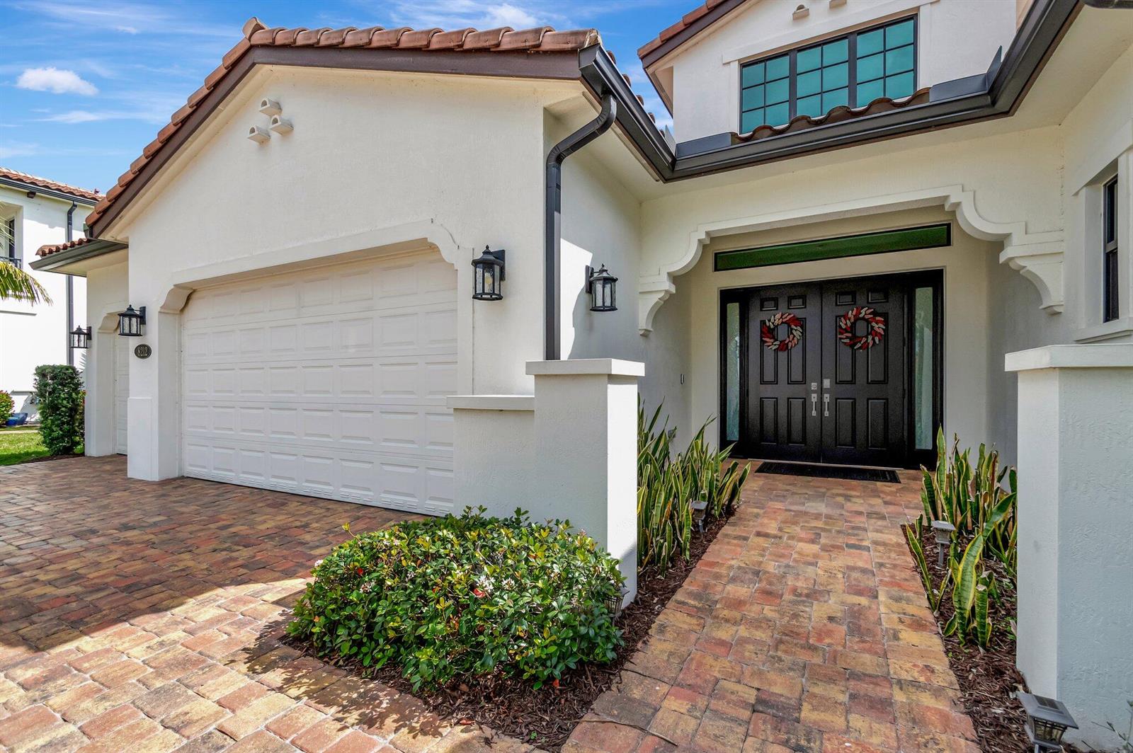 The exterior of a house features a brick driveway, a garage, and a double front door — 8212 Grand Prix Lane, Boynton Beach FL 33472, BOYNTON BEACH, FL