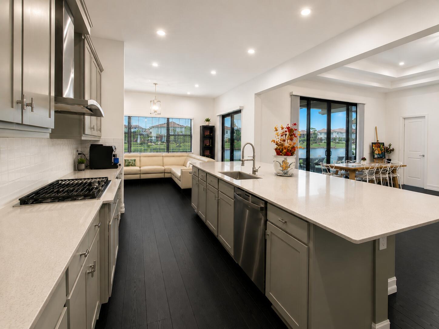 A modern kitchen with gray cabinets, white countertops, and dark wood floors overlooks a living area — 8212 Grand Prix Lane, Boynton Beach FL 33472, BOYNTON BEACH, FL