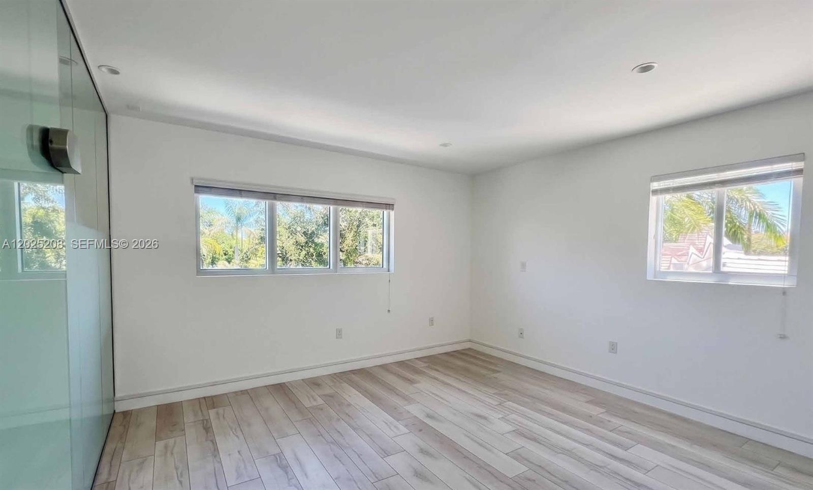 An empty room features white walls, light wood-look flooring, and two windows with blinds — 6320 Biscayne Blvd, Miami FL 33138, MIAMI, FL
