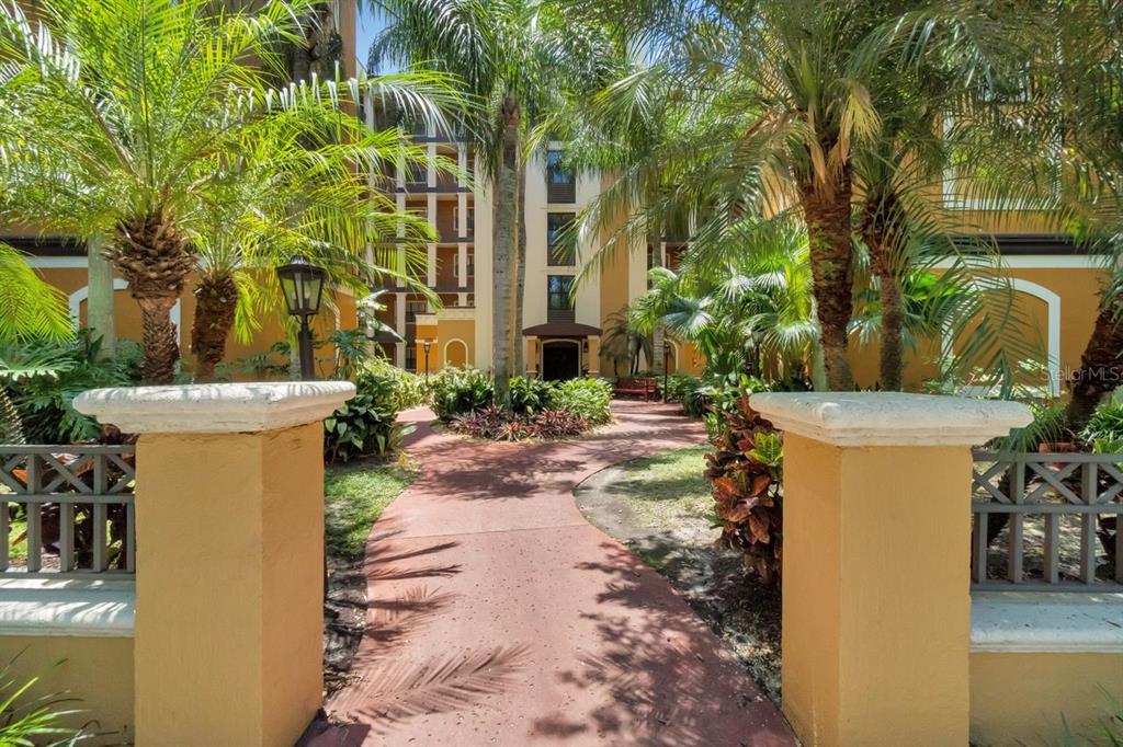 A paved walkway leads through a tropical courtyard toward the entrance of a multi-story building — 12538 FLORIDAYS RESORT DRIVE UNIT 511C, ORLANDO, FL
