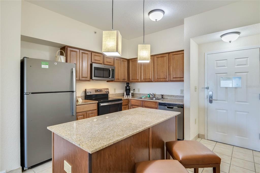 A kitchen features wood cabinets, granite countertops, stainless steel appliances, and a central island — 12538 FLORIDAYS RESORT DRIVE UNIT 511C, ORLANDO, FL