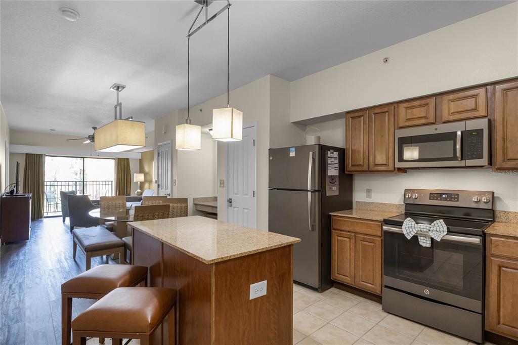 A kitchen with wood cabinets, stainless steel appliances, and an island opens to a dining area — 12538 FLORIDAYS RESORT DRIVE UNIT 511C, ORLANDO, FL