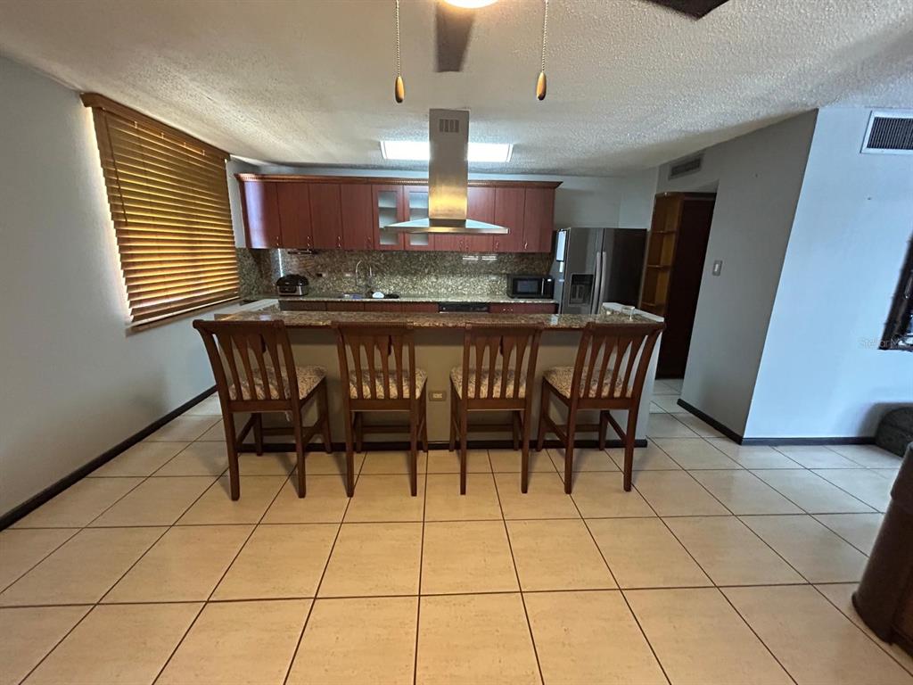 A kitchen features wooden cabinets, a granite breakfast bar with four chairs, and tile flooring — Cond Esmeralda #7 CALLE AMAPOLA UNIT 602, CAROLINA, PR