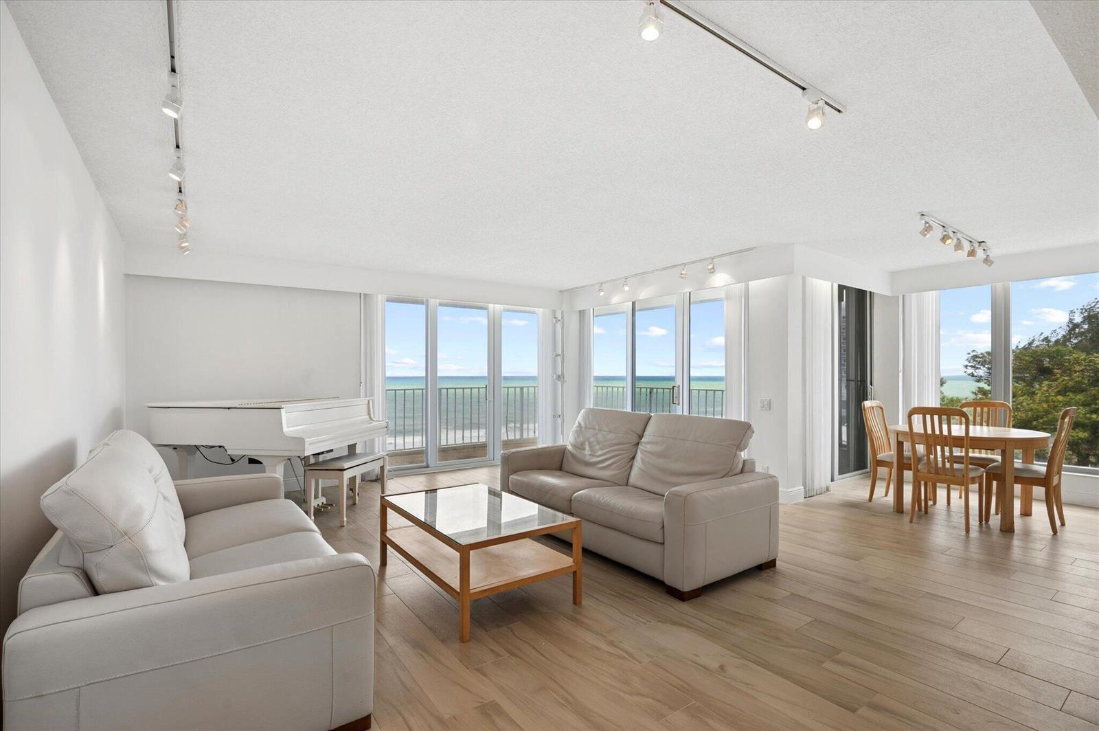 A bright living and dining area features white sofas, a piano, and ocean views — 1010 S Ocean Boulevard # 501, Pompano Beach FL 33062, POMPANO BEACH, FL