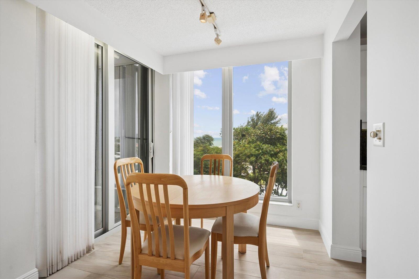 A dining area with a round wooden table, four chairs, and large windows overlooking trees — 1010 S Ocean Boulevard # 501, Pompano Beach FL 33062, POMPANO BEACH, FL