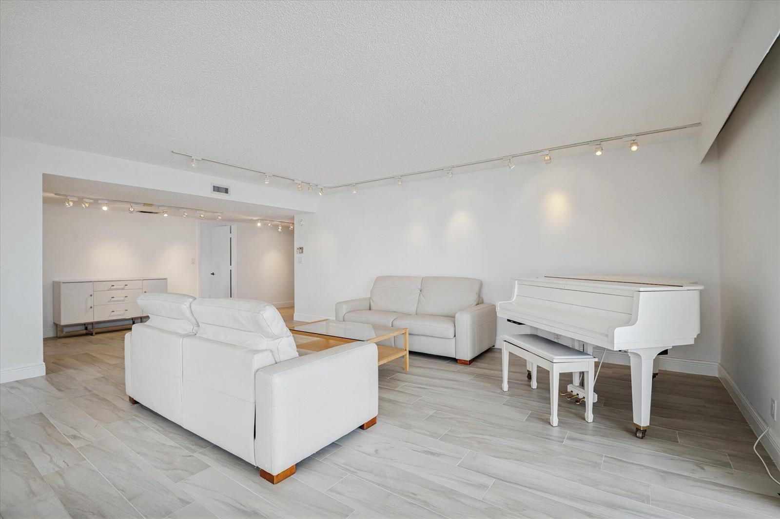 A bright living room features white leather sofas, a white grand piano, and light flooring — 1010 S Ocean Boulevard # 501, Pompano Beach FL 33062, POMPANO BEACH, FL