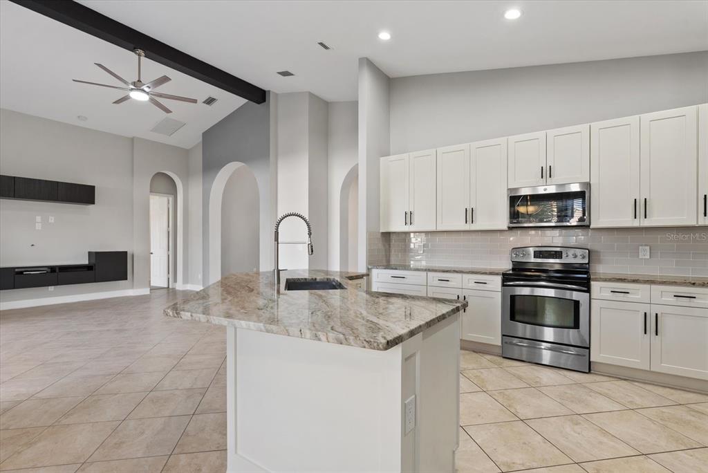 A kitchen with white cabinets, granite countertops, and a central island opens to a living area — 6634 38TH STREET E, SARASOTA, FL