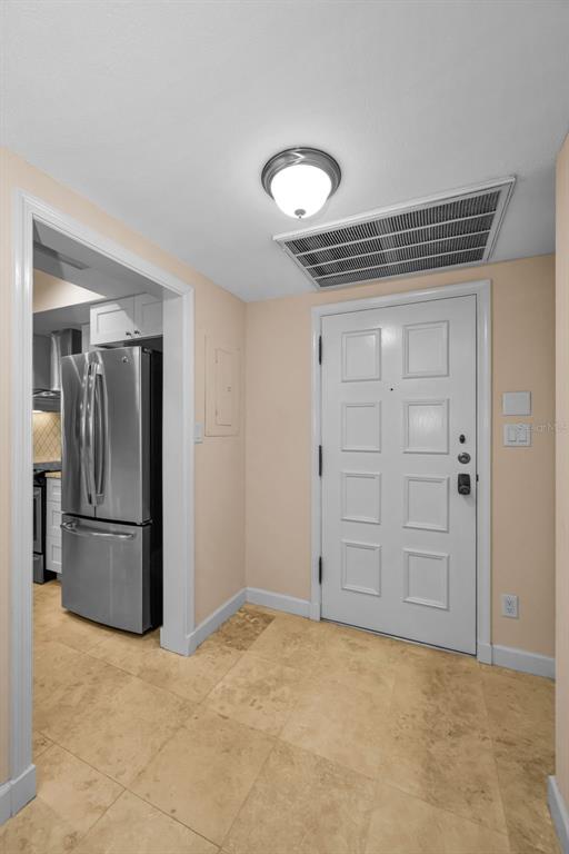 An entryway with beige tile flooring leads to a white door and a stainless refrigerator — 36750 US HIGHWAY 19 UNIT 26-102, PALM HARBOR, FL