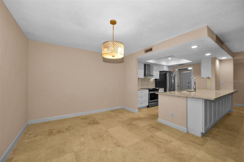 A dining area with a pendant light opens into a kitchen with white cabinets and counters — 36750 US HIGHWAY 19 UNIT 26-102, PALM HARBOR, FL