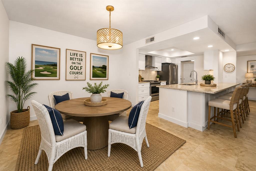 A dining area with a round wooden table and white chairs sits beside a kitchen — 36750 US HIGHWAY 19 UNIT 26-102, PALM HARBOR, FL