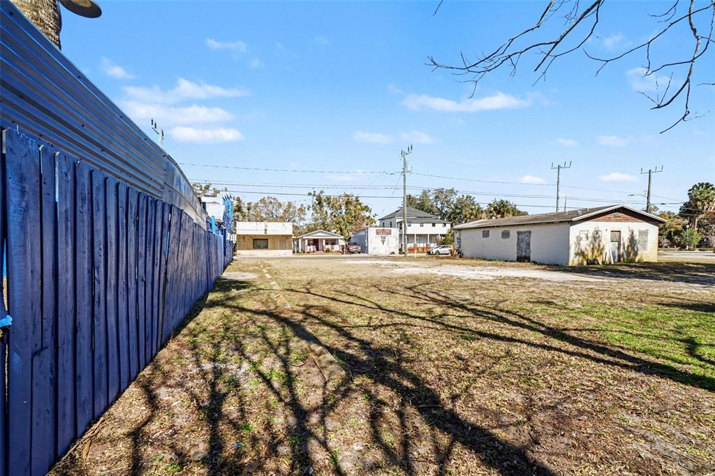 A vacant dirt lot sits between a blue fence and a small, light-colored building — 1013 HISTORIC GOLDSBORO BOULEVARD, SANFORD, FL