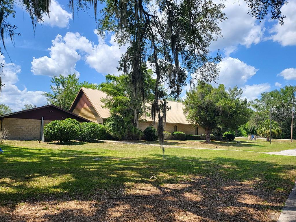A tan-roofed building with stone walls sits on a grassy lot with Spanish moss trees — 1990 SE HIGHWAY 42 UNIT 1, SUMMERFIELD, FL