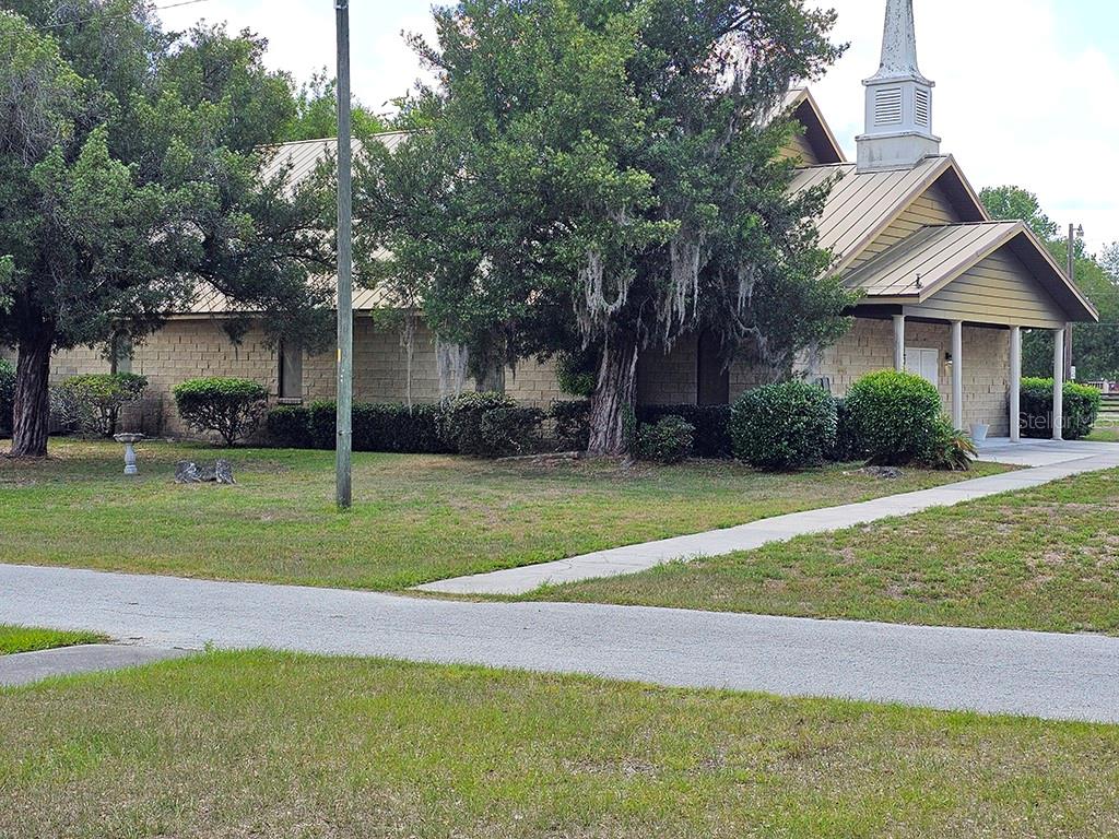 A tan, single-story church building with a metal roof and a steeple sits on grass — 1990 SE HIGHWAY 42 UNIT 1, SUMMERFIELD, FL