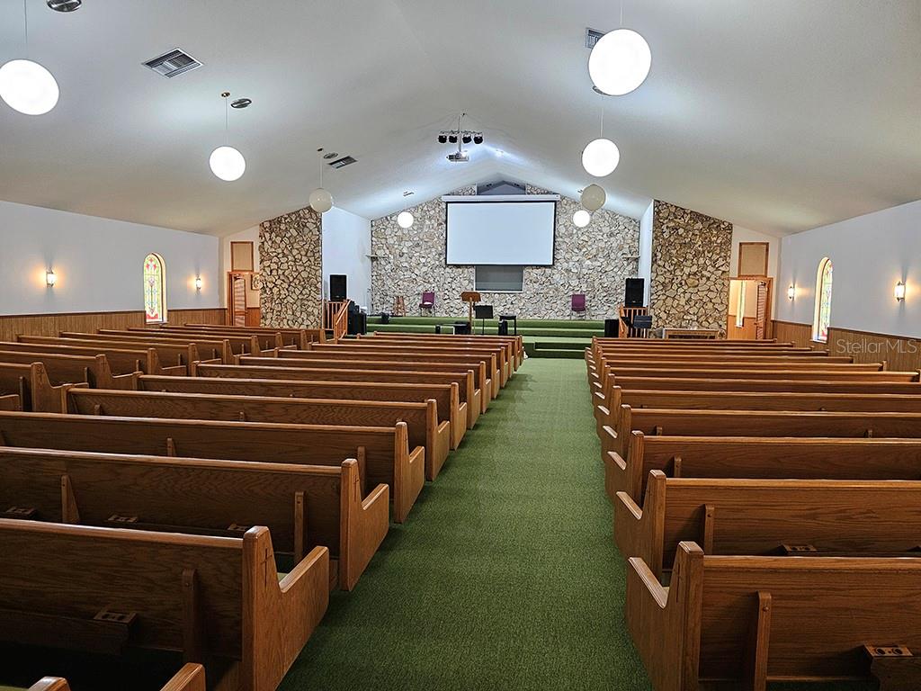 A church sanctuary features rows of wooden pews, green carpeting, and a stone-accented stage area — 1990 SE HIGHWAY 42 UNIT 1, SUMMERFIELD, FL