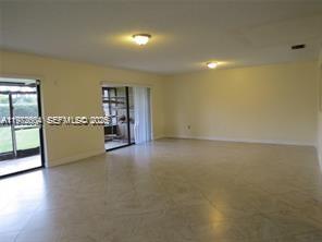 An empty living room with light-colored tile flooring, two ceiling lights, and sliding glass doors — 216 Lakeside Cir, Sunrise FL 33326, SUNRISE, FL