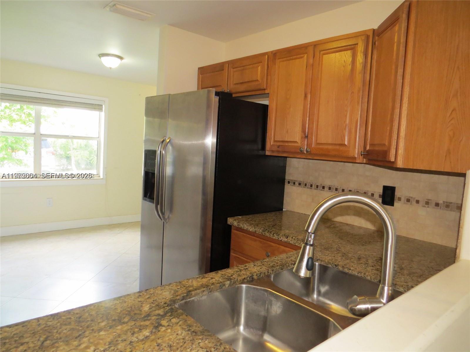 A kitchen features wood cabinets, granite countertops, a stainless steel sink, and a refrigerator — 216 Lakeside Cir, Sunrise FL 33326, SUNRISE, FL