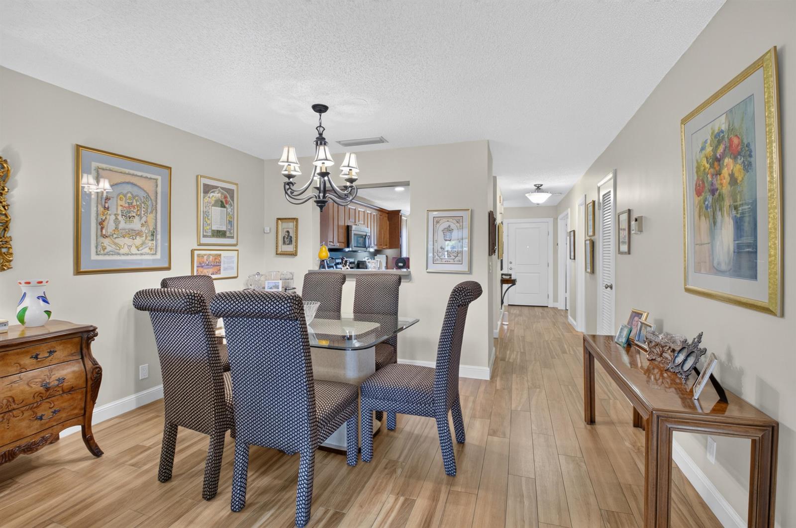 A dining room features a glass-top table, patterned chairs, wood-look flooring, and framed wall art — 5896 Via Delray Boulevard # A, Delray Beach FL 33484, DELRAY BEACH, FL
