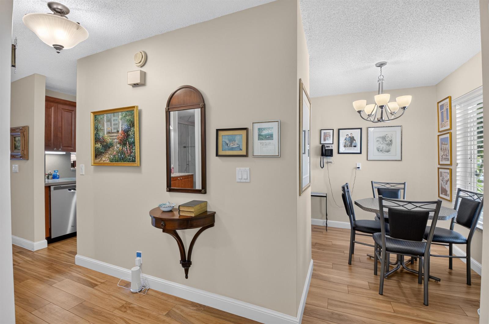 A dining area and kitchen entrance feature light walls, wood-look flooring, and traditional wall decor — 5896 Via Delray Boulevard # A, Delray Beach FL 33484, DELRAY BEACH, FL