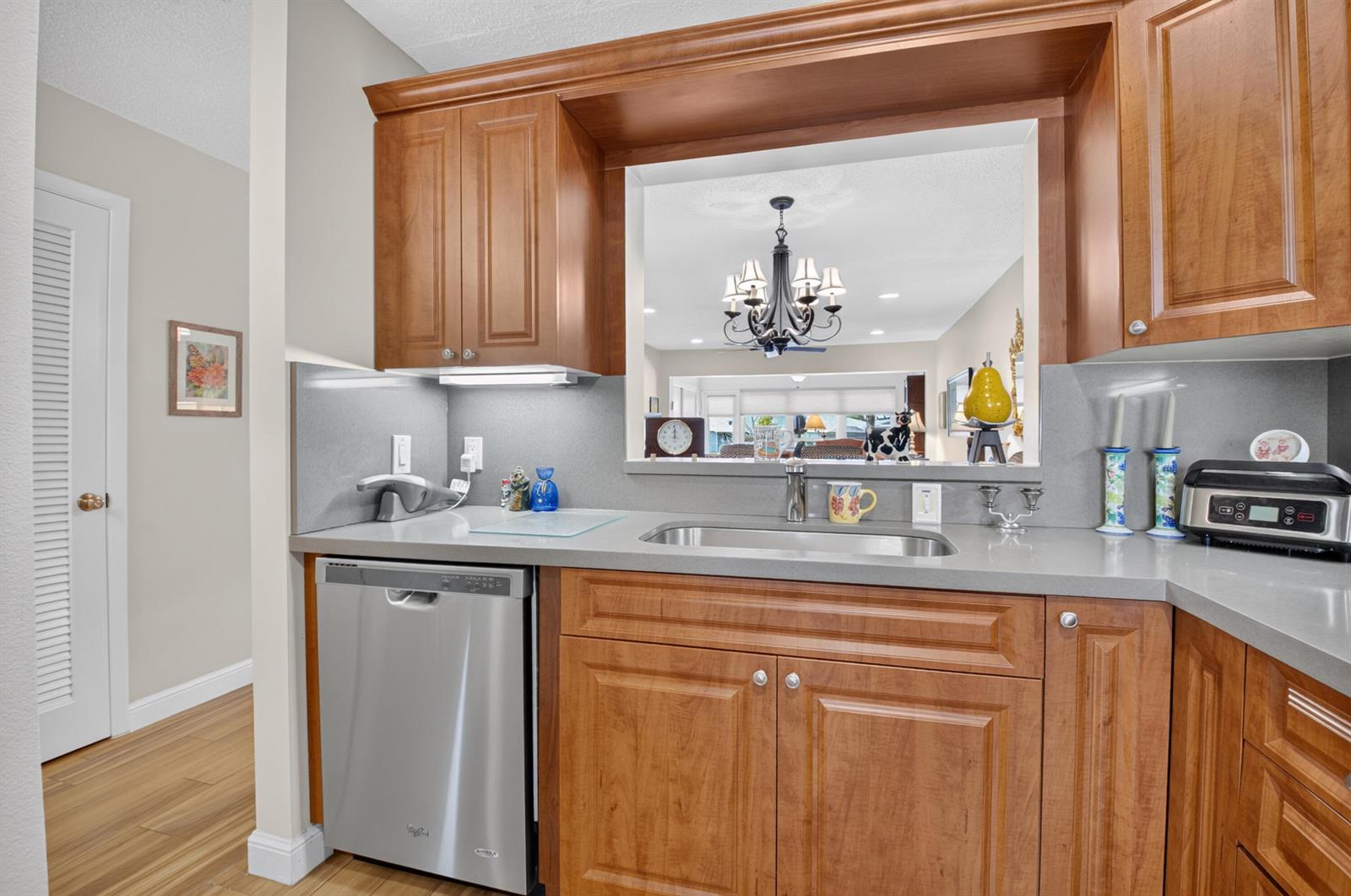 A kitchen features wood cabinets, a stainless steel dishwasher, a sink, and a pass-through window — 5896 Via Delray Boulevard # A, Delray Beach FL 33484, DELRAY BEACH, FL