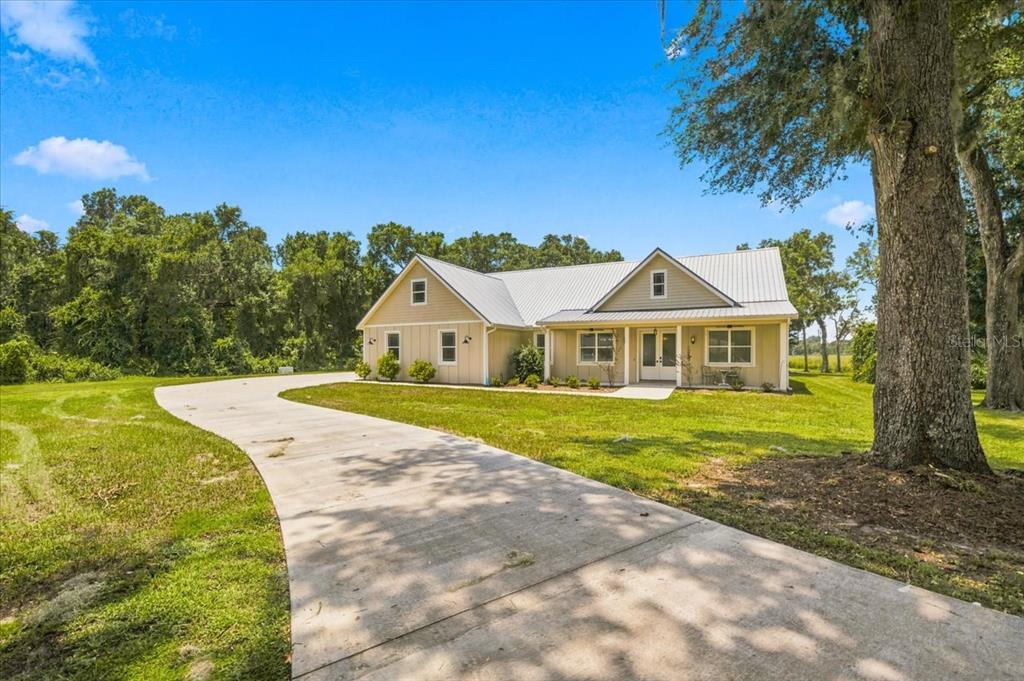 A tan single-story house with a metal roof sits at the end of a concrete driveway — 32 N SHADOW WOOD DRIVE, INVERNESS, FL
