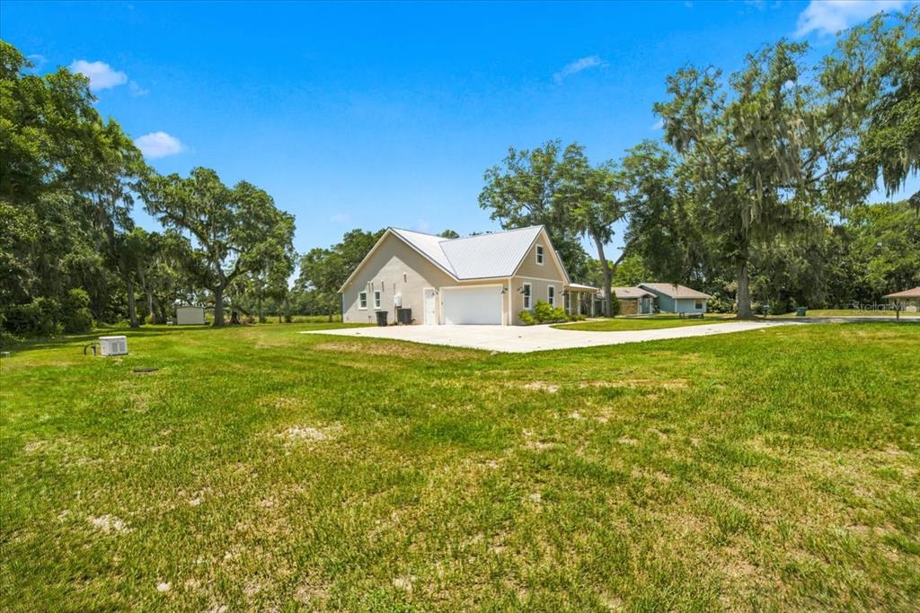 A tan house with a metal roof and a large concrete driveway sits on grass — 32 N SHADOW WOOD DRIVE, INVERNESS, FL