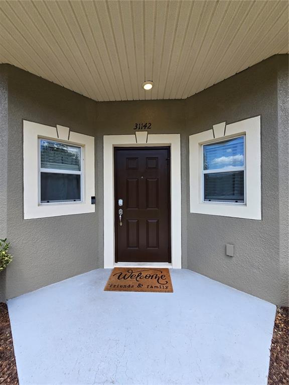A brown front door is centered between two windows on a gray stucco porch — 31142 GOSSAMER WAY, WESLEY CHAPEL, FL