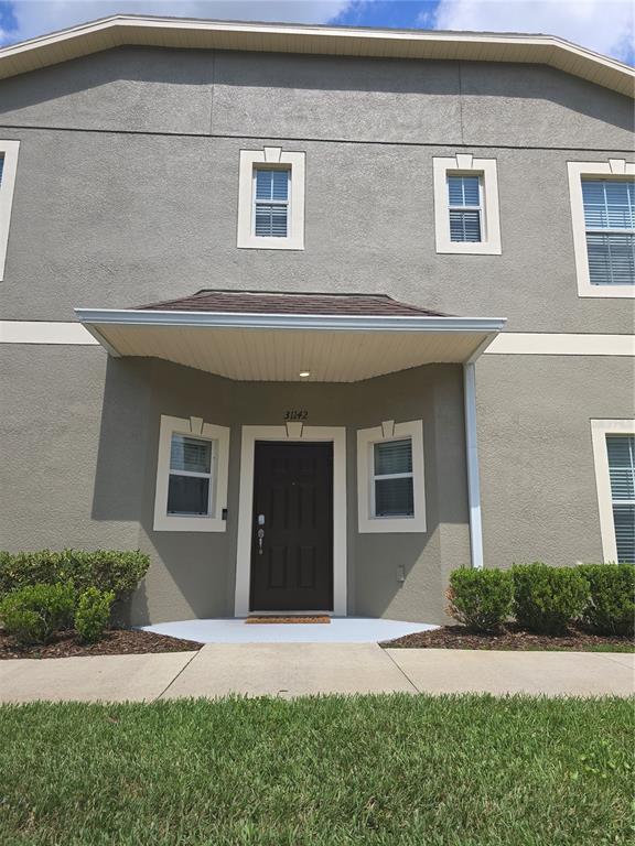 The exterior of a two-story stucco townhouse features a dark front door under a canopy — 31142 GOSSAMER WAY, WESLEY CHAPEL, FL