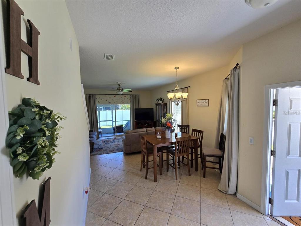An open-concept dining and living area features tile flooring, a wooden table, and sliding doors — 31142 GOSSAMER WAY, WESLEY CHAPEL, FL
