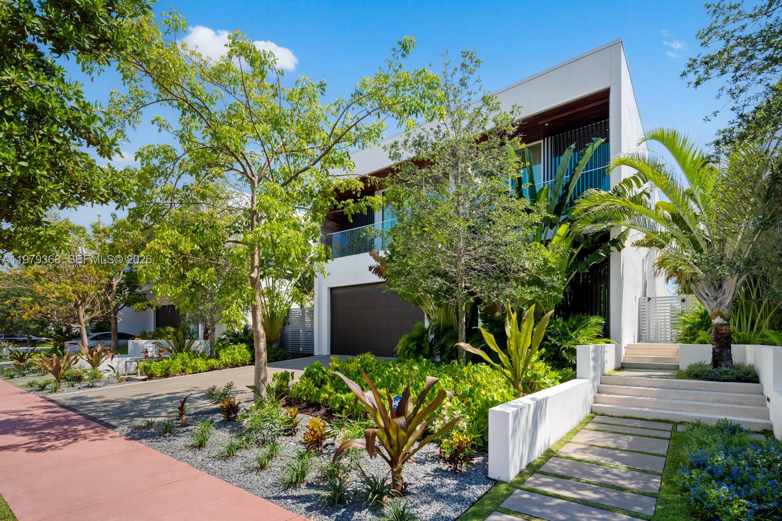 A modern two-story house with a dark garage door, glass balconies, and landscaped front yard — 1051 W 48th St # 4, Miami Beach FL 33140, MIAMI BEACH, FL