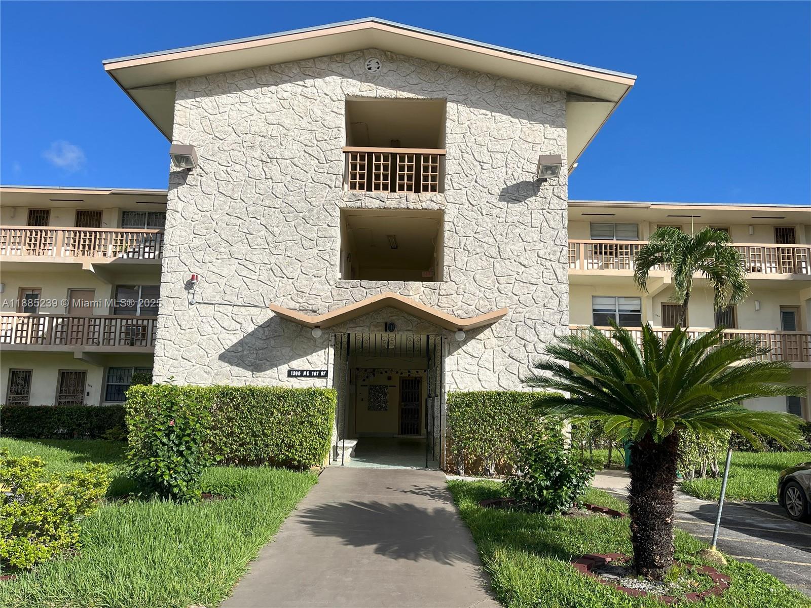 A three-story apartment building features a stone facade, a central entrance, and balconies with railings — 1395 NE 167th St # 315, Miami FL 33162, MIAMI, FL