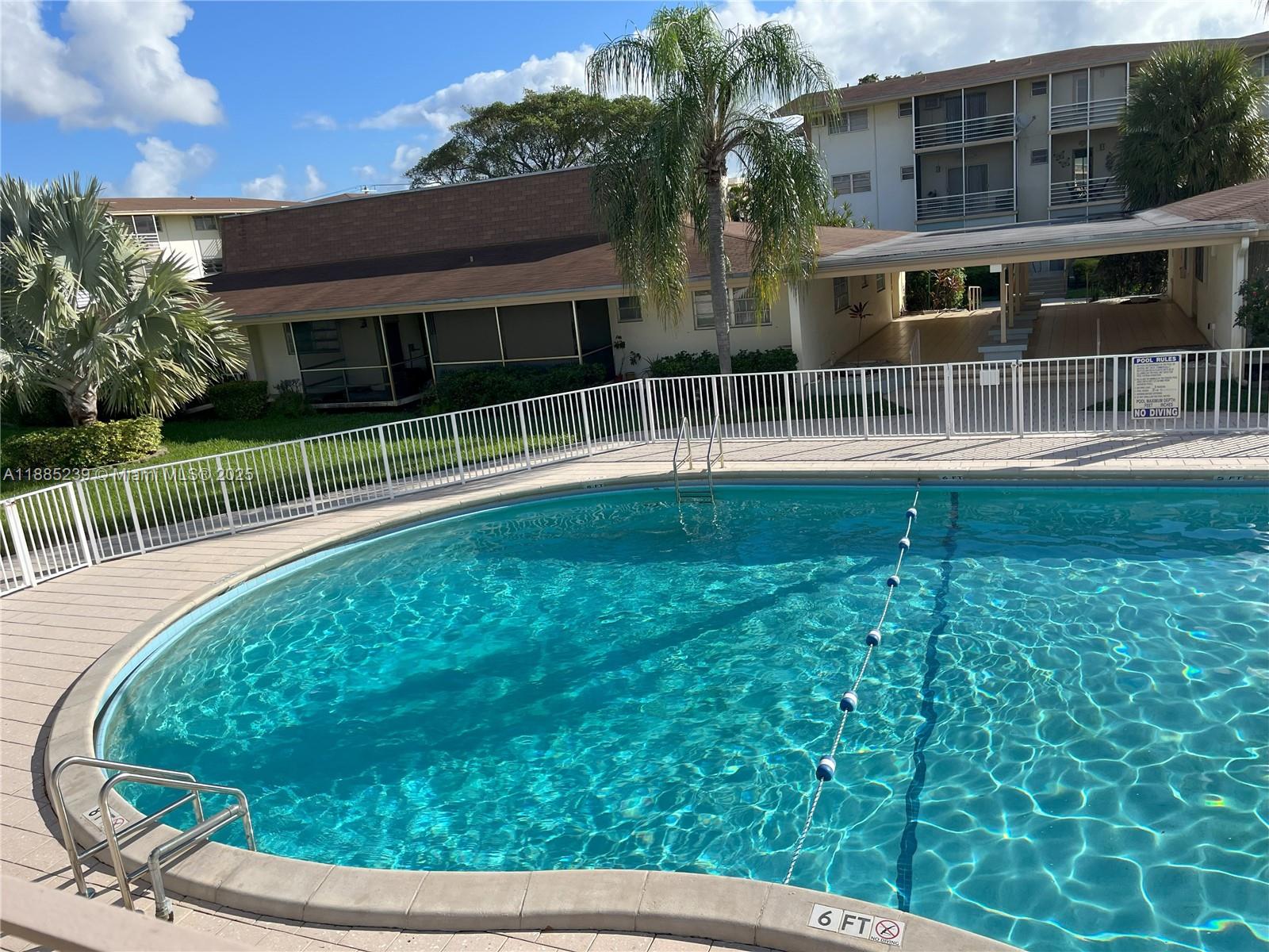A swimming pool with a safety rope and metal ladder sits in front of apartment buildings — 1395 NE 167th St # 315, Miami FL 33162, MIAMI, FL