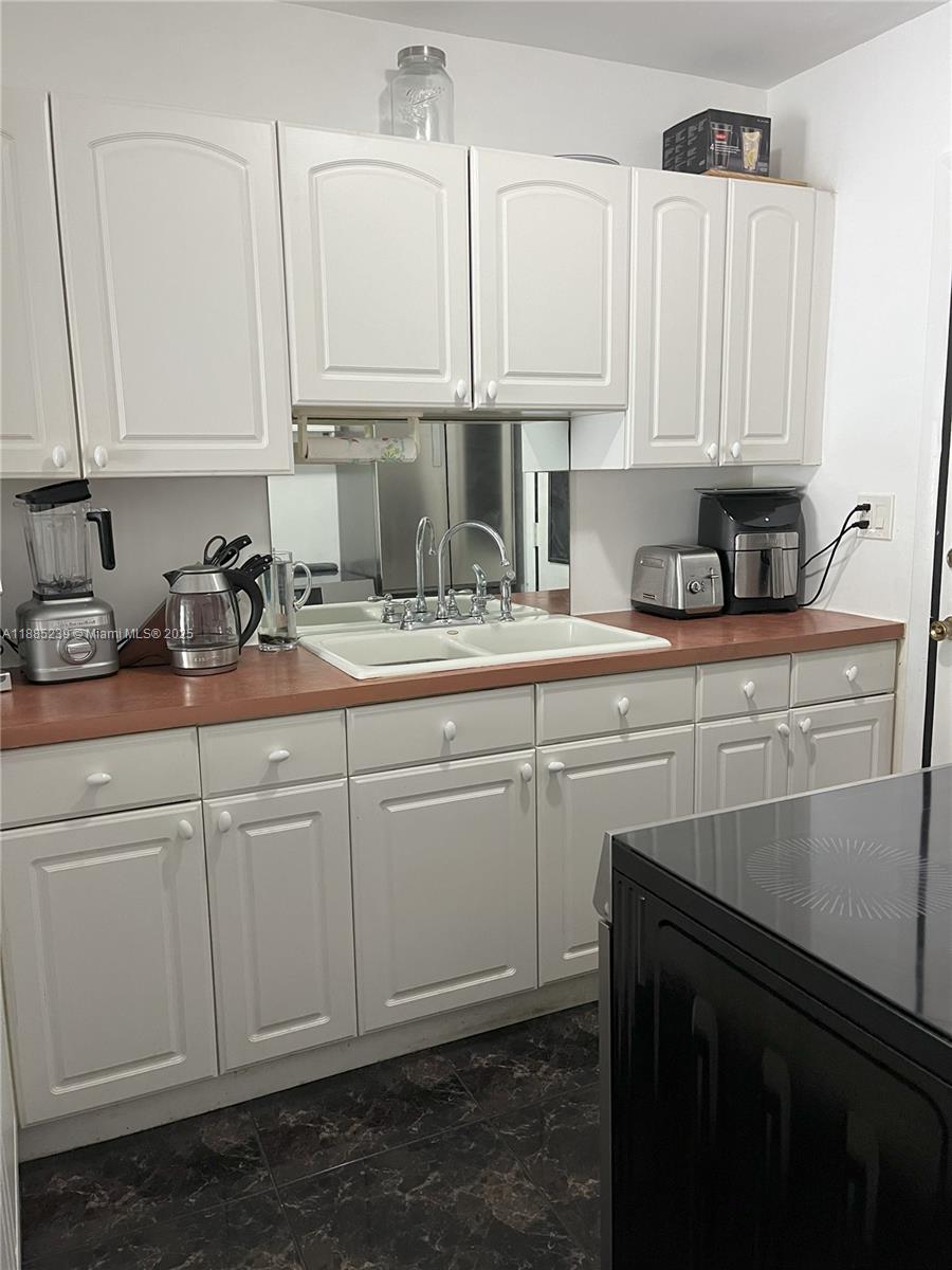 A kitchen features white cabinets, a reddish-brown countertop, a double sink, and black appliances — 1395 NE 167th St # 315, Miami FL 33162, MIAMI, FL