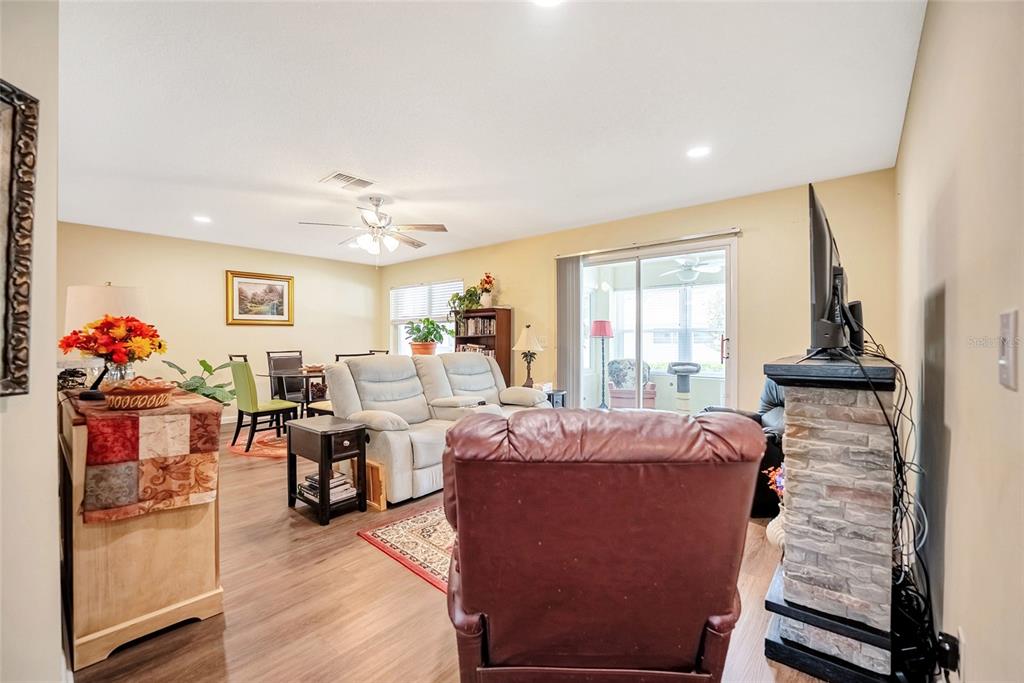 A living room features wood-look flooring, a stone-faced television stand, and a sliding glass door — 9685 SW 97TH STREET, OCALA, FL