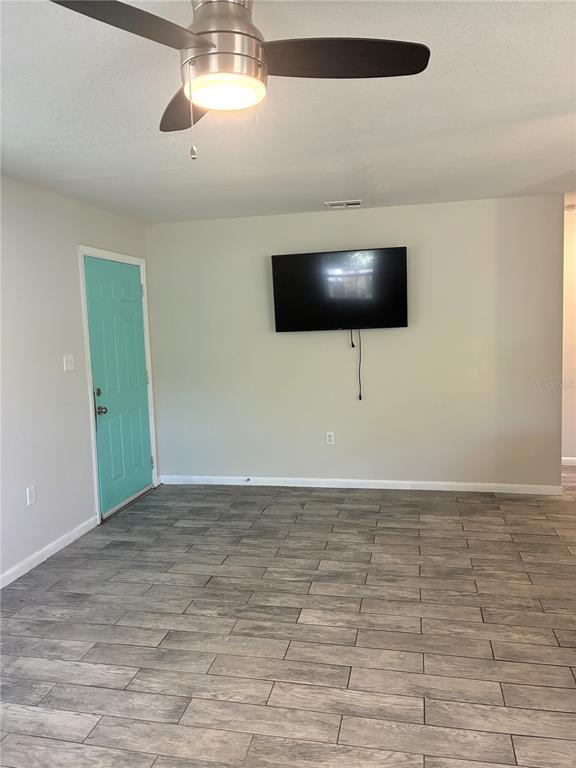 A living room features gray wood-look tile flooring, a ceiling fan, and a wall-mounted television — 618 4TH AVENUE NE, LARGO, FL