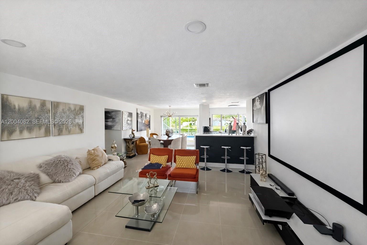 A living room features a large projection screen, white sofa, orange chairs, and a breakfast bar — 8085 NW 21st St, Sunrise FL 33322, SUNRISE, FL