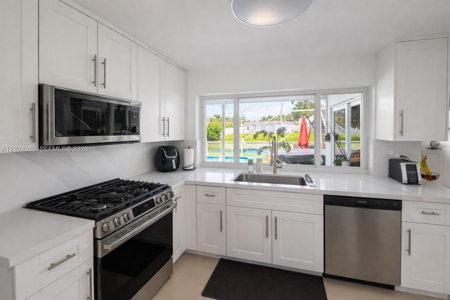 A white kitchen features stainless steel appliances, quartz countertops, and a window overlooking a pool — 8085 NW 21st St, Sunrise FL 33322, SUNRISE, FL