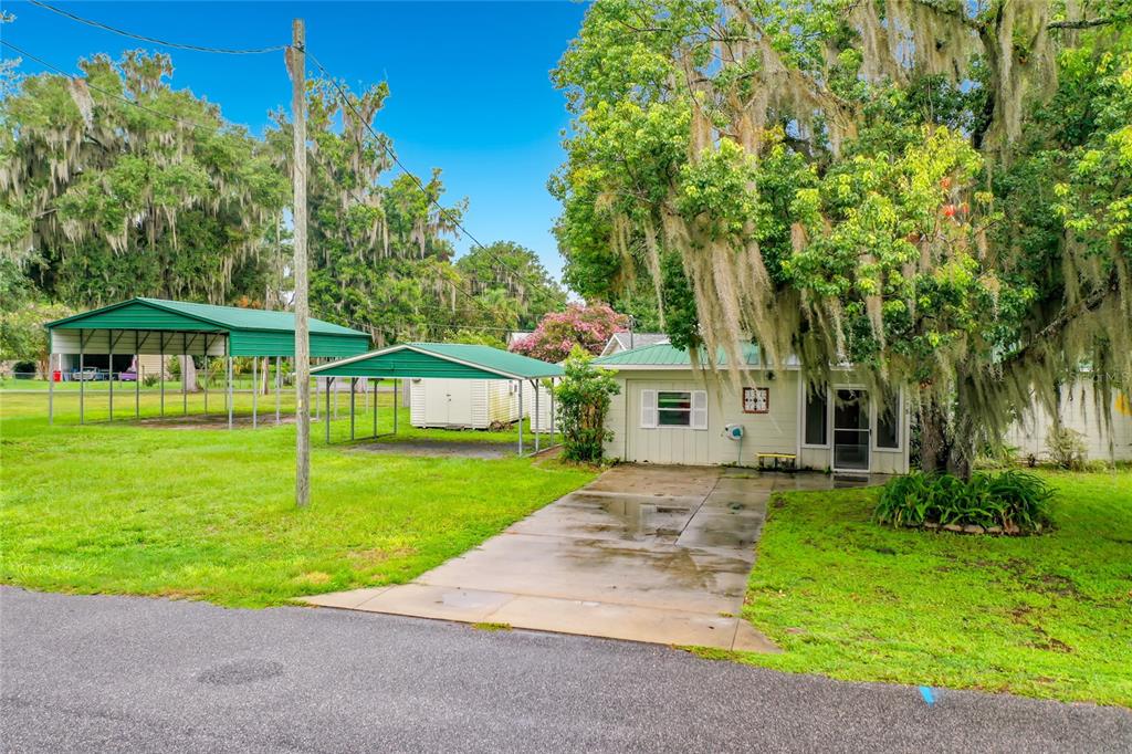 A small house with a concrete driveway, two metal carports, and large moss-covered trees — 1218 CR 450, LAKE PANASOFFKEE, FL