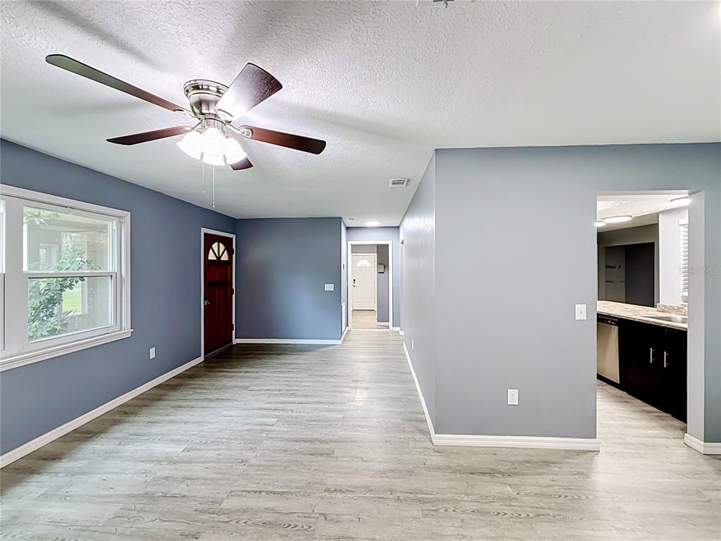 A living room with gray walls, wood-look flooring, a ceiling fan, and an adjacent kitchen — 1218 CR 450, LAKE PANASOFFKEE, FL