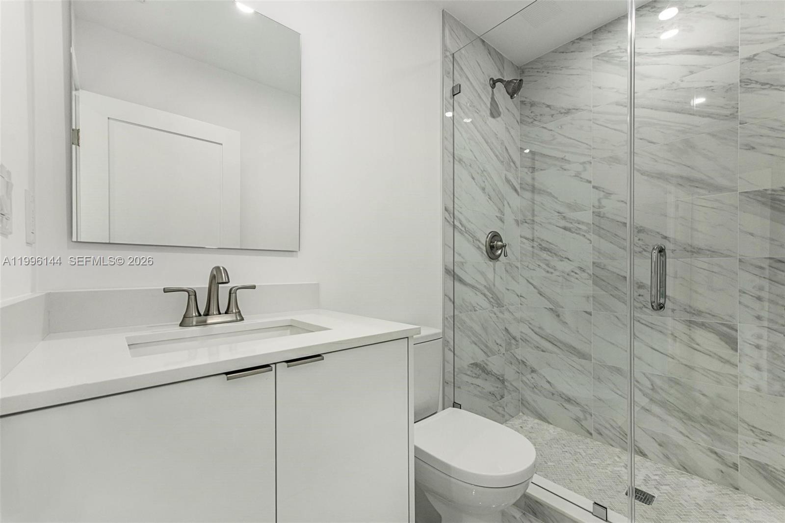A modern bathroom features a white vanity, a marble-tiled walk-in shower, and a toilet — 10370 SW 24th St # B, Miami FL 33165, MIAMI, FL