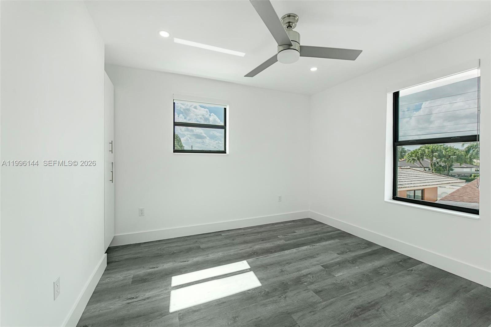 An empty bedroom features white walls, gray wood-look flooring, a ceiling fan, and two windows — 10370 SW 24th St # B, Miami FL 33165, MIAMI, FL