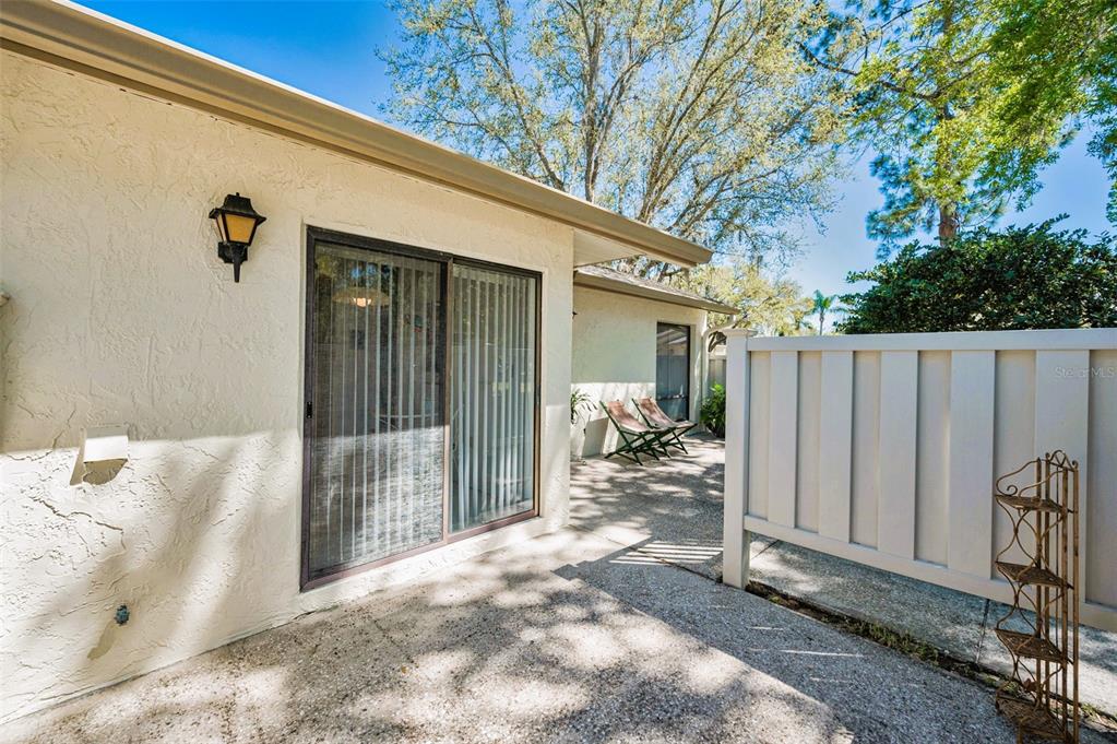 A concrete patio features a sliding glass door, a privacy fence, and two folding chairs — 1333 SHADY PINE WAY UNIT F, TARPON SPRINGS, FL