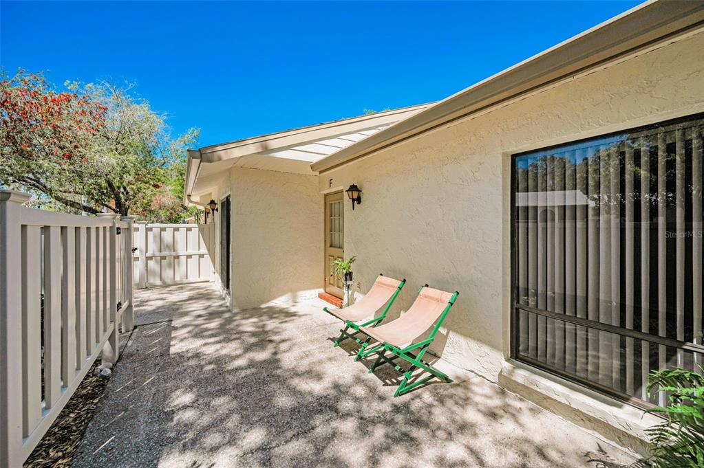 A patio with two folding chairs sits outside the entrance of a tan stucco building — 1333 SHADY PINE WAY UNIT F, TARPON SPRINGS, FL