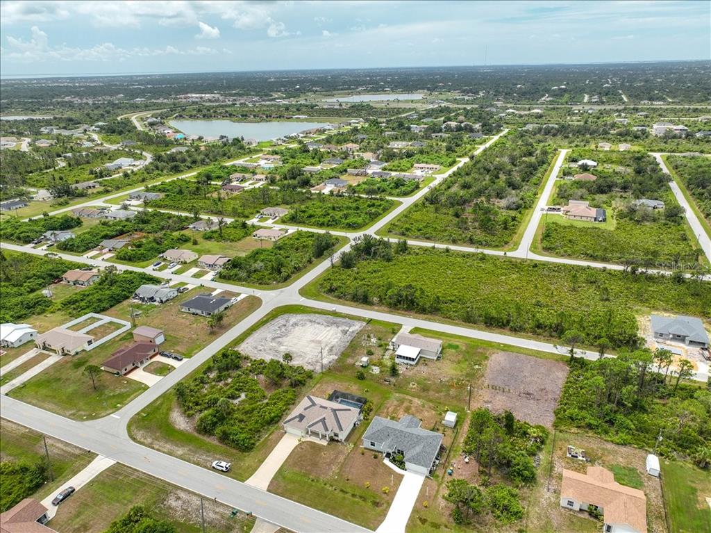 An aerial view shows a suburban neighborhood with scattered houses, vacant lots, and a lake — 11707 WILLMINGTON BOULEVARD, PORT CHARLOTTE, FL
