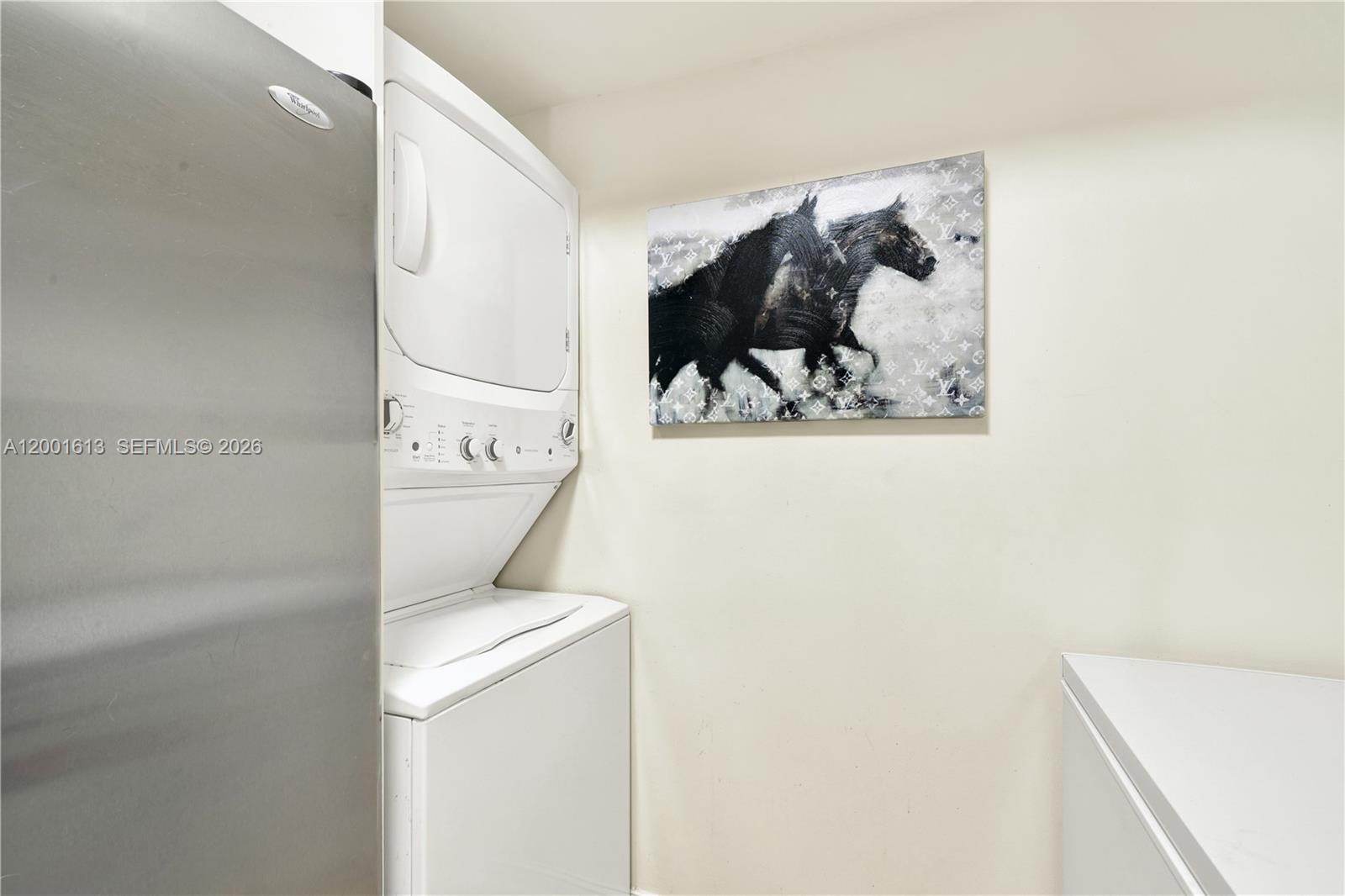 A laundry area features a stacked washer and dryer unit next to a wall painting — 5077 NW 7th St # 508, Miami FL 33126, MIAMI, FL
