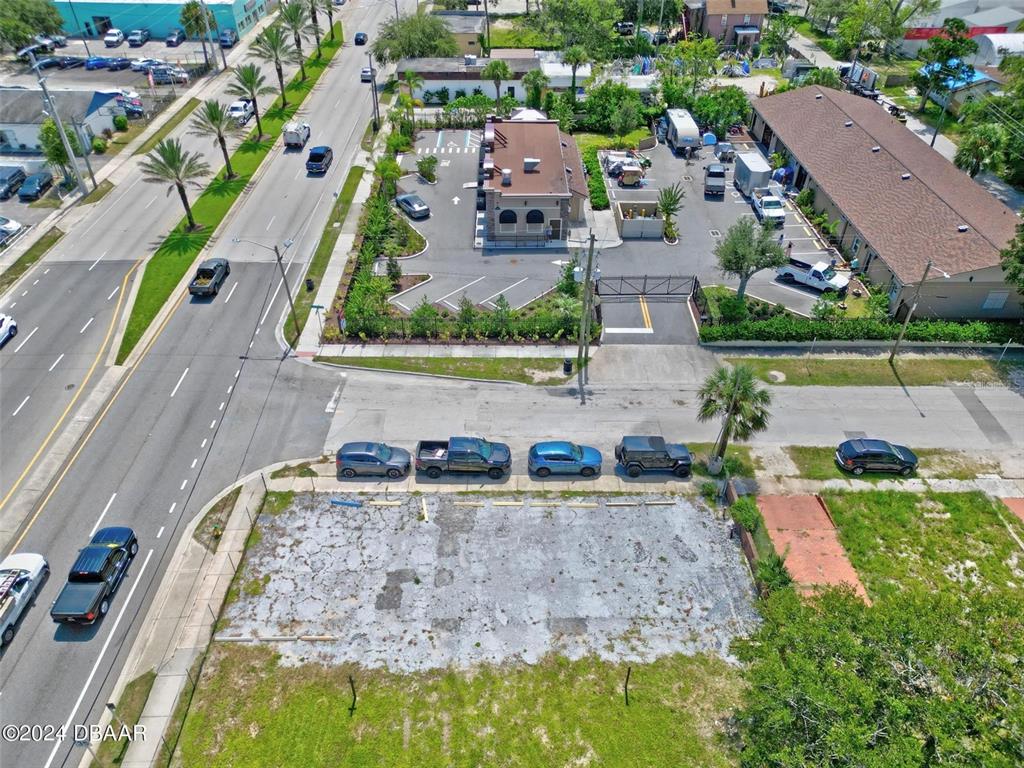 An aerial view shows a vacant, paved lot adjacent to a street and commercial buildings — RIDGEWOOD AVENUE, DAYTONA BEACH, FL