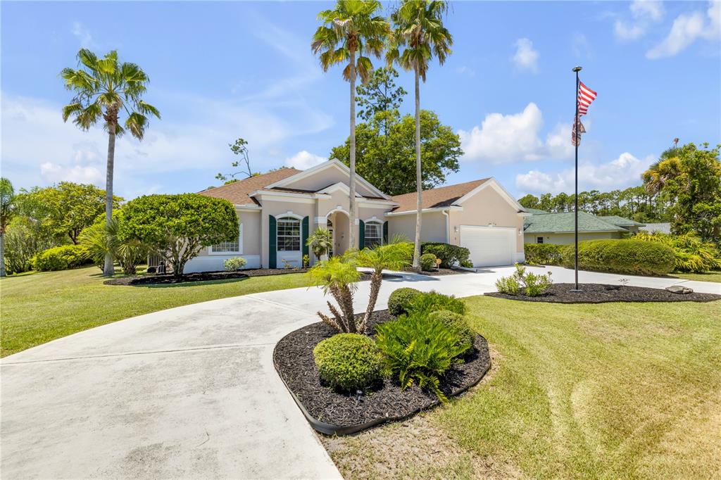 A single-story house with a beige exterior, a concrete driveway, and palm trees in front — 1 WELLINGTON DRIVE, PALM COAST, FL