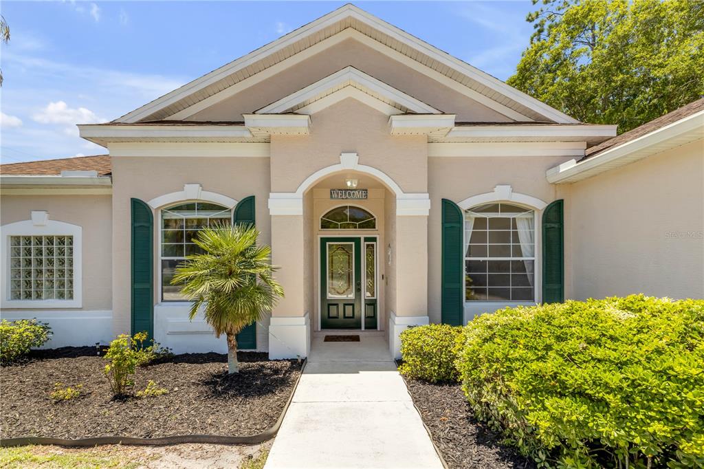 The exterior of a single-story house features a front entrance with a green door and shutters — 1 WELLINGTON DRIVE, PALM COAST, FL