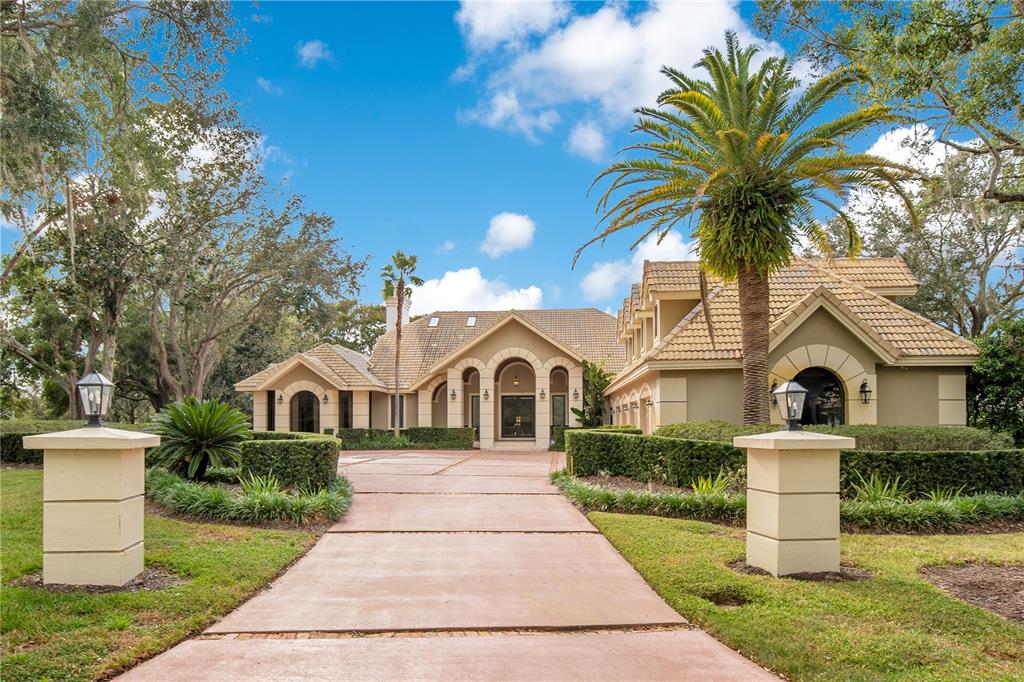 A paved driveway leads to the front entrance of a tan house with a palm tree — 5524 WORSHAM COURT, WINDERMERE, FL