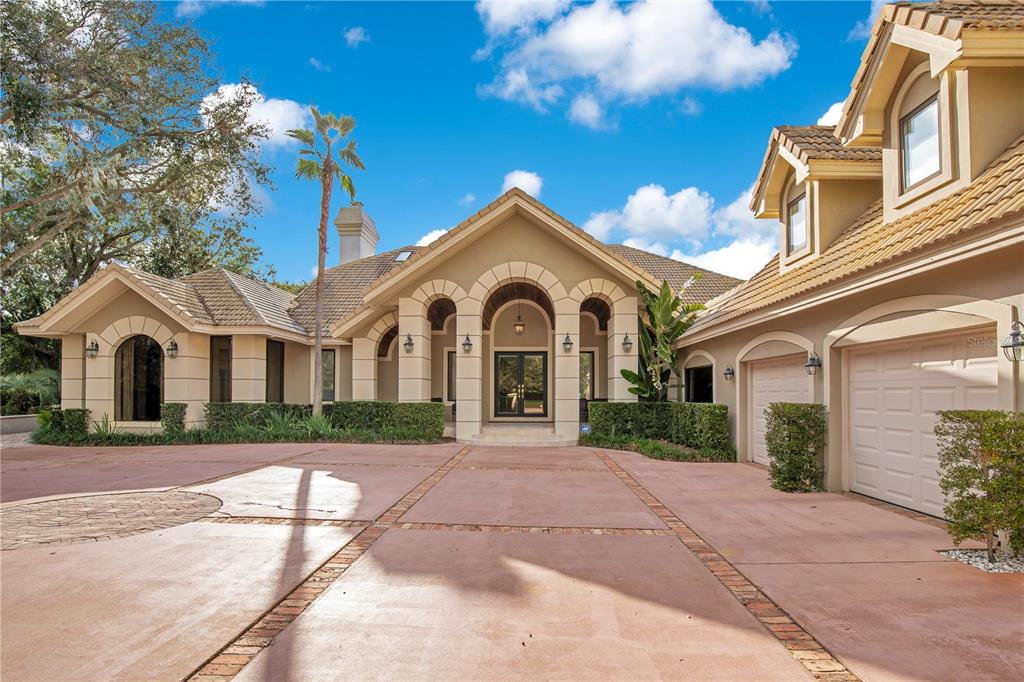 A tan stucco house with a tiled roof, arched entryway, and a large paved driveway — 5524 WORSHAM COURT, WINDERMERE, FL